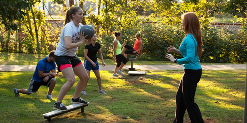 Group using balance and coordination outdoor fitness equipment in a park training session